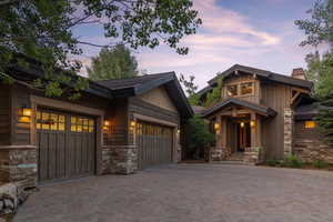 Craftsman-style home featuring stone siding, decorative driveway, a garage, a chimney, and board and batten siding