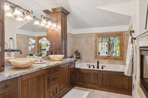 Full bath with double vanity, a bath, light tile patterned flooring, tile walls, and vaulted ceiling