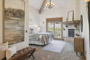 Bedroom featuring beam ceiling, carpet floors, access to exterior, a glass covered fireplace, and a chandelier