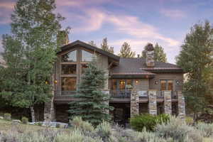 Back of house at dusk featuring stone siding, a chimney, and a balcony