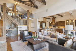 Living area with beam ceiling, wood finished floors, a chandelier, high vaulted ceiling, and stairs