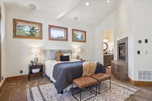 Carpeted bedroom featuring connected bathroom, beam ceiling, high vaulted ceiling, and a fireplace