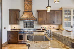 Kitchen with decorative backsplash, double oven range, light wood finished floors, and premium range hood