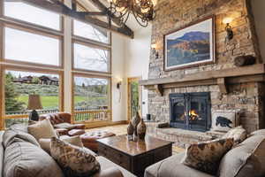 Living room featuring high vaulted ceiling, a chandelier, wood finished floors, and a stone fireplace