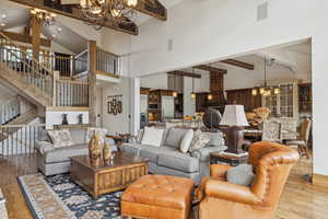 Living room with a chandelier, beamed ceiling, wood finished floors, stairway, and high vaulted ceiling