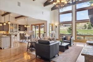 Living area with a chandelier, beam ceiling, light wood finished floors, and a high ceiling