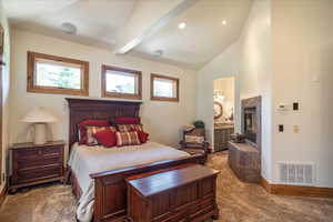 Bedroom featuring carpet flooring, vaulted ceiling, a tiled fireplace, and ensuite bath