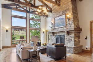 Living area featuring high vaulted ceiling, light wood-style flooring, a fireplace, beamed ceiling, and a chandelier