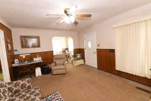 Carpeted living area featuring wainscoting, wood walls, arched walkways, and ceiling fan