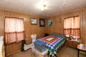 Carpeted bedroom with wood walls and a textured ceiling