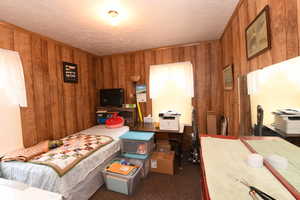 Carpeted bedroom featuring wood walls and a textured ceiling