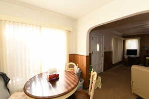 Carpeted dining room with arched walkways, wood walls, and a wainscoted wall