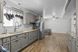 Kitchen featuring gray cabinetry, ceiling fan, freestanding refrigerator, wood finished floors, and light stone countertops