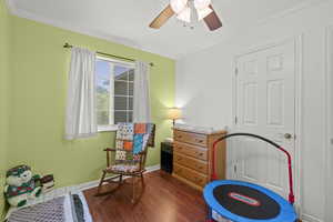Playroom with dark wood finished floors, ornamental molding, and ceiling fan