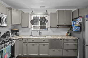 Kitchen featuring gray cabinets, appliances with stainless steel finishes, decorative backsplash, and light stone countertops
