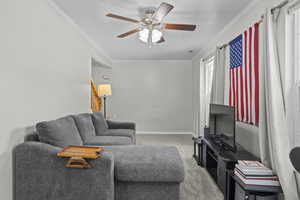 Living area featuring carpet, crown molding, a ceiling fan, and stairway
