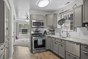 Kitchen featuring stainless steel appliances, gray cabinetry, light wood-style floors, a ceiling fan, and tasteful backsplash