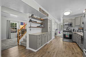 Kitchen featuring gray cabinets, stainless steel appliances, ornamental molding, wood finished floors, and light stone countertops