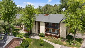 Back of house featuring a balcony, stucco siding, roof with shingles, and a yard