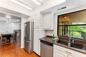 Kitchen with stainless steel appliances, light wood-style flooring, white cabinetry, and dark stone counters