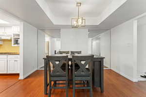 Dining area with wood finished floors, a raised ceiling, and a chandelier