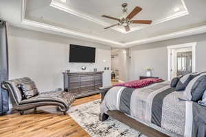 Bedroom with a raised ceiling, crown molding, wood finished floors, arched walkways, and recessed lighting