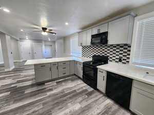 Kitchen featuring black appliances, gray cabinets, a peninsula, wood finished floors, and tasteful backsplash
