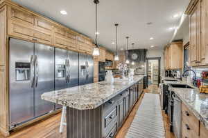 Kitchen with light wood-style flooring, a large island, backsplash, light stone countertops, and stainless steel appliances