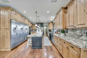 Kitchen featuring stainless steel appliances, light brown cabinetry, light stone countertops, a breakfast bar area, and a center island