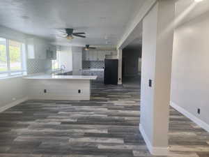 Kitchen featuring black fridge, light countertops, a peninsula, ceiling fan, and dark wood-type flooring