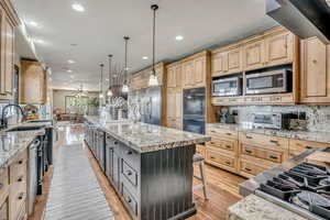 Kitchen with appliances with stainless steel finishes, light brown cabinetry, a large island, recessed lighting, and a breakfast bar