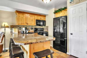 Kitchen with black appliances, a kitchen breakfast bar, a peninsula, backsplash, and light brown cabinetry