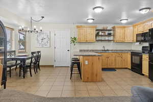 Kitchen featuring light tile patterned floors, a textured ceiling, a breakfast bar area, open shelves, and black appliances