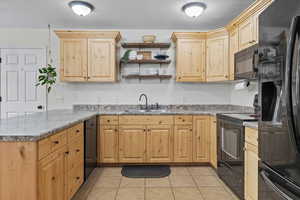 Kitchen featuring black appliances, open shelves, light brown cabinetry, light tile patterned floors, and a peninsula