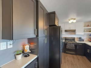 Kitchen featuring black appliances, under cabinet range hood, open shelves, light countertops, and a textured ceiling