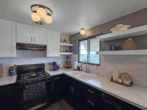 Kitchen with black range with gas cooktop, open shelves, under cabinet range hood, dishwasher, and a textured ceiling