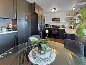 Kitchen with black appliances, under cabinet range hood, light countertops, a textured ceiling, and open shelves