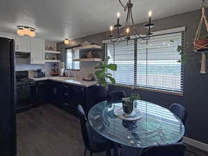 Kitchen with black appliances, open shelves, a textured ceiling, a chandelier, and under cabinet range hood