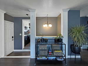 Entrance foyer with a textured ceiling, decorative columns, wood finished floors, and a chandelier