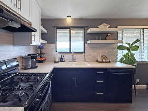Kitchen featuring black appliances, under cabinet range hood, light countertops, backsplash, and a textured ceiling