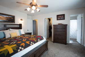 Bedroom with a walk in closet, light colored carpet, a closet, ensuite bath, and a ceiling fan