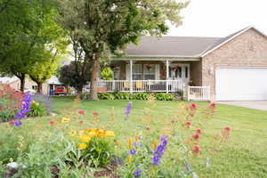 Ranch-style house with a porch, an attached garage, brick siding, a front yard, and driveway