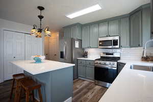 Kitchen featuring appliances with stainless steel finishes, dark wood-style floors, tasteful backsplash, a kitchen island, and light countertops