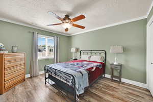 Bedroom with wood finished floors, ornamental molding, a textured ceiling, and a ceiling fan