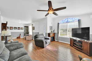 Living room featuring a ceiling fan, lofted ceiling, and light wood finished floors