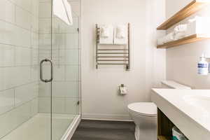 Bathroom with radiator, wood finished floors, a shower stall, vanity, and a towel warmer
