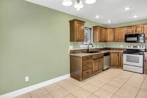 Kitchen with stainless steel appliances, light tile patterned flooring, brown cabinets, and recessed lighting