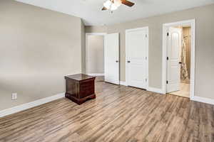 Primary bedroom with wood finished floors, ensuite bathroom, and a ceiling fan