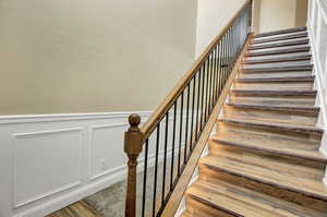 Stairs featuring wainscoting, wood finished floors, and a decorative wall with a lights.