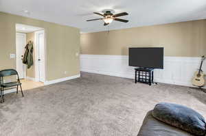 Carpeted living area featuring ceiling fan and wainscoting